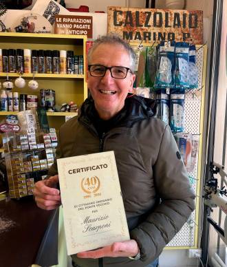 Maurizio Scarponi nel suo negozio, alle spalle l’insegna storica del suo maestro