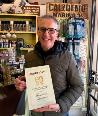 Maurizio Scarponi nel suo negozio, alle spalle l’insegna storica del suo maestro